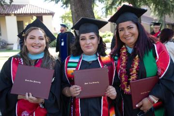 Graduates in regalia pose with their diplomas 