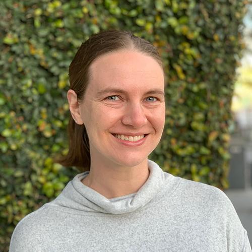 A person smiling in front of a leafy background.