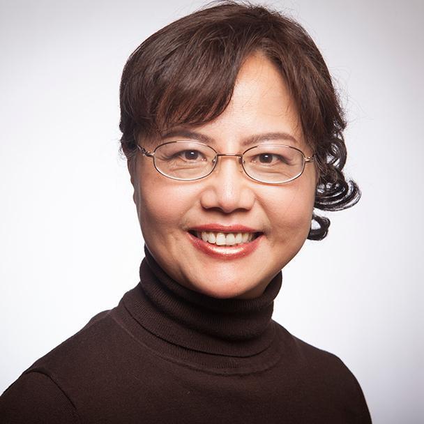 A person smiling, wearing glasses and a dark top.