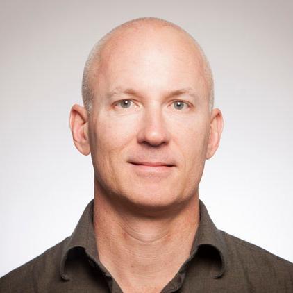 A man in a dark shirt against a plain background.