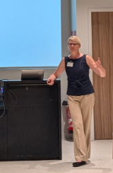 Birgit Koopmann-Holm standing next to podium and presenting.