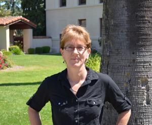 Person wearing glasses and a black shirt standing outdoors near a tree.