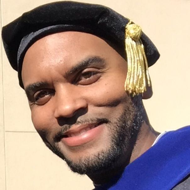 A man in graduation attire smiling at the camera.
