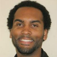 A man smiling in a black shirt, titled