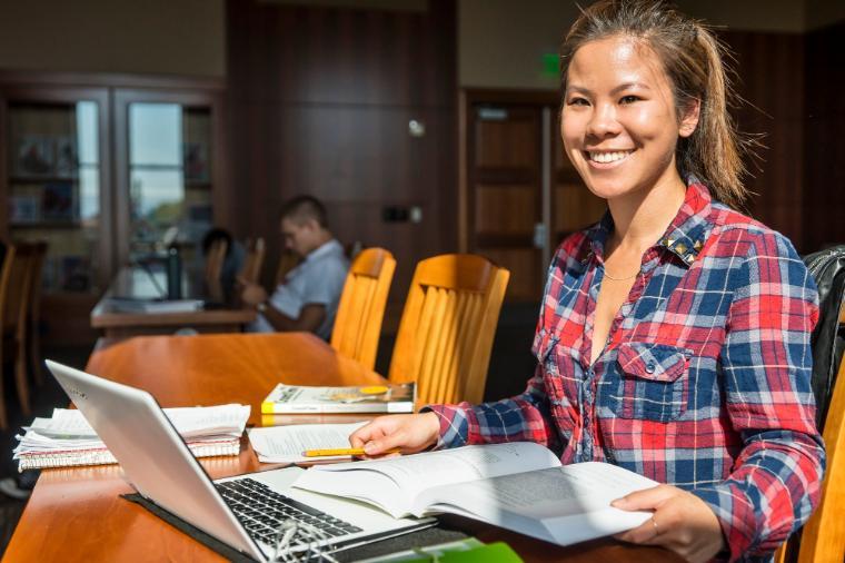 A student studying with her laptop and papers on a wood table 