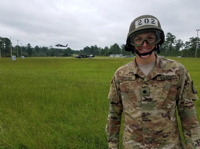 A soldier wearing camouflage gear and helmet standing in a grassy field.