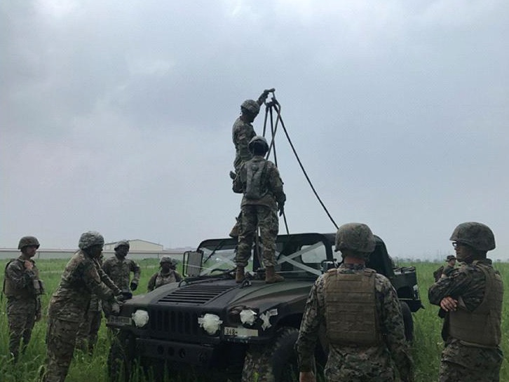 Soldiers gathered around a vehicle in a field.