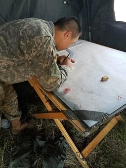 Person in military uniform working on a map or document.