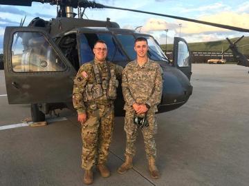 Two soldiers in uniform standing in front of a helicopter.
