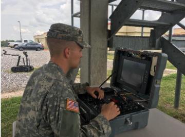 Person in military attire operating a computer outdoors under covered area.
