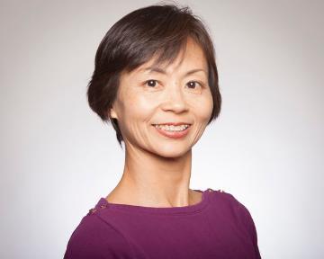 A person smiling, wearing a purple top, with a white background.