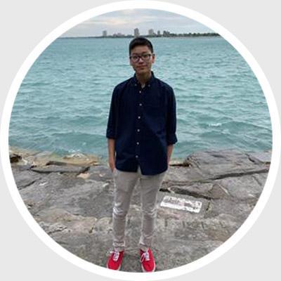 Person standing near a large body of water, with a rocky shoreline in the background.