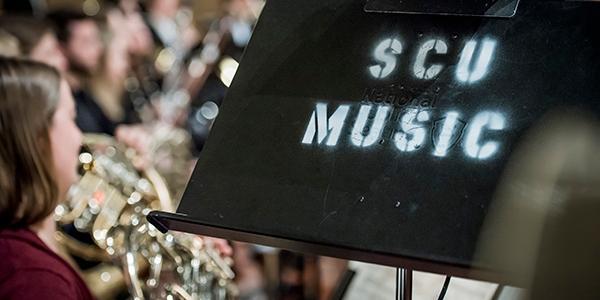 Zoom in of a music stand with SCU Music on it with students playing in the background 