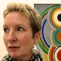 A person with a patterned scarf in front of colorful wall art.