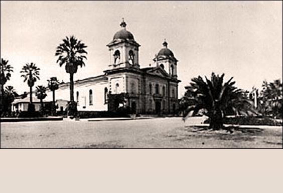 Historic building with two towers and palm trees, titled 