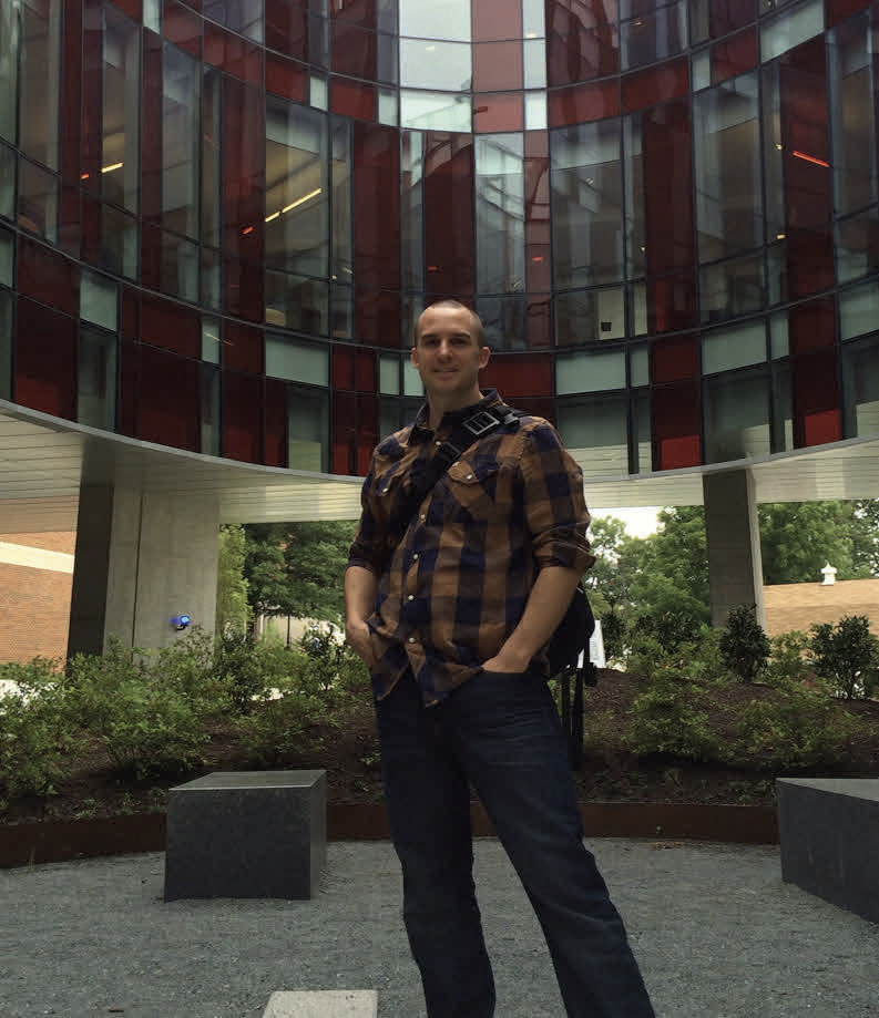 A person standing in a spacious indoor area with plants and tall windows.