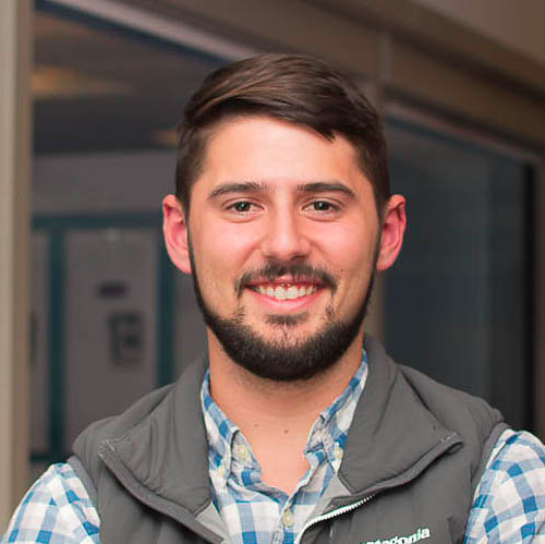 A person wearing a vest over a checked shirt smiling.