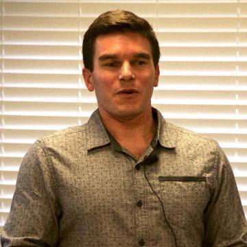 A person standing indoors in front of blinds.