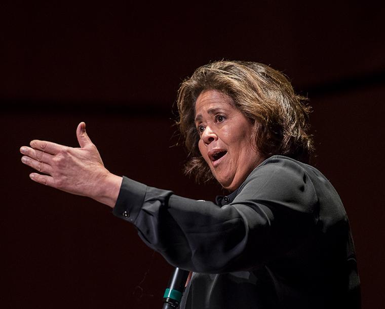 A person speaking animatedly, with an outstretched hand.