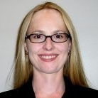 A person with glasses, smiling in front of a plain background.