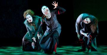 Three performers in dramatic poses on dimly lit stage. 