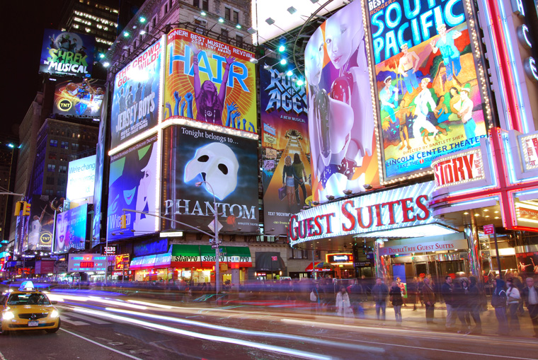 Times Square at night with brightly lit Broadway theatre billboards.