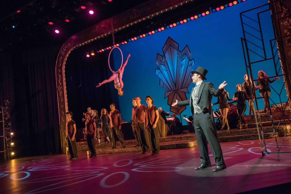 Stage performance with aerial act and dancers in the background.