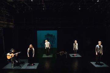 Five people perform on stage in dim lighting.