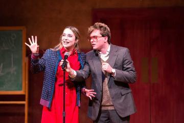 Two people on stage speaking into microphones during the