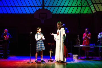 A child and an adult on stage, colorful spotlights overhead.