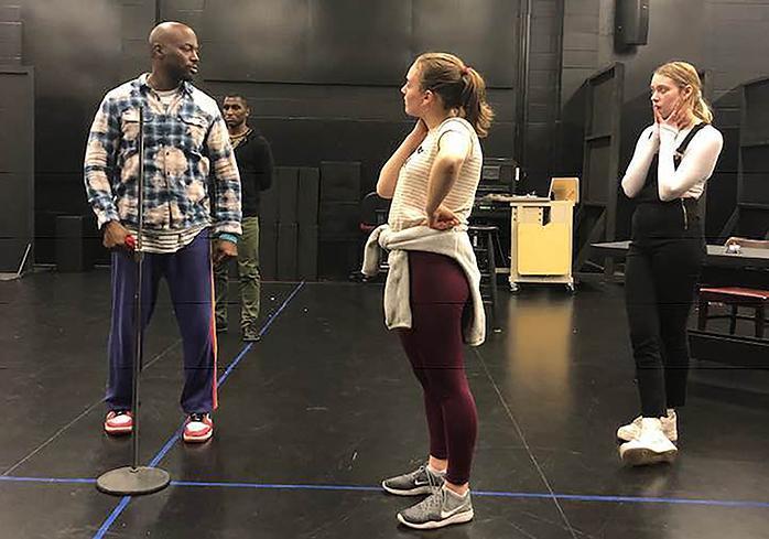 Three people rehearsing on a stage, including one person in floral shirt.