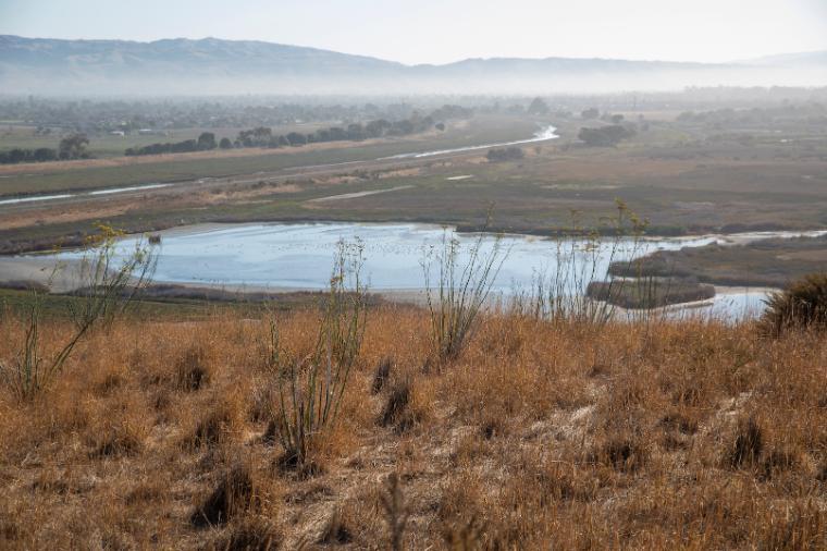 photograph of landscape featuring dry grasses and a body of water amongst hills