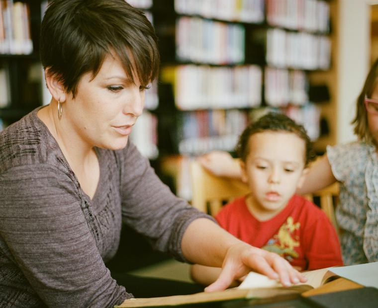 Alt text: Teacher helping a young student in a classroom setting.