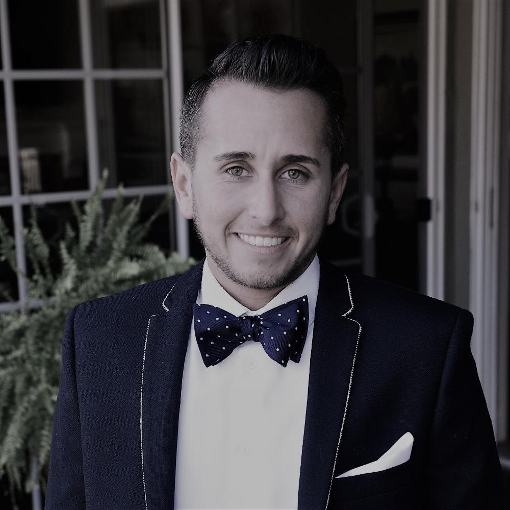 A person in formal attire with a bowtie and jacket, standing indoors.