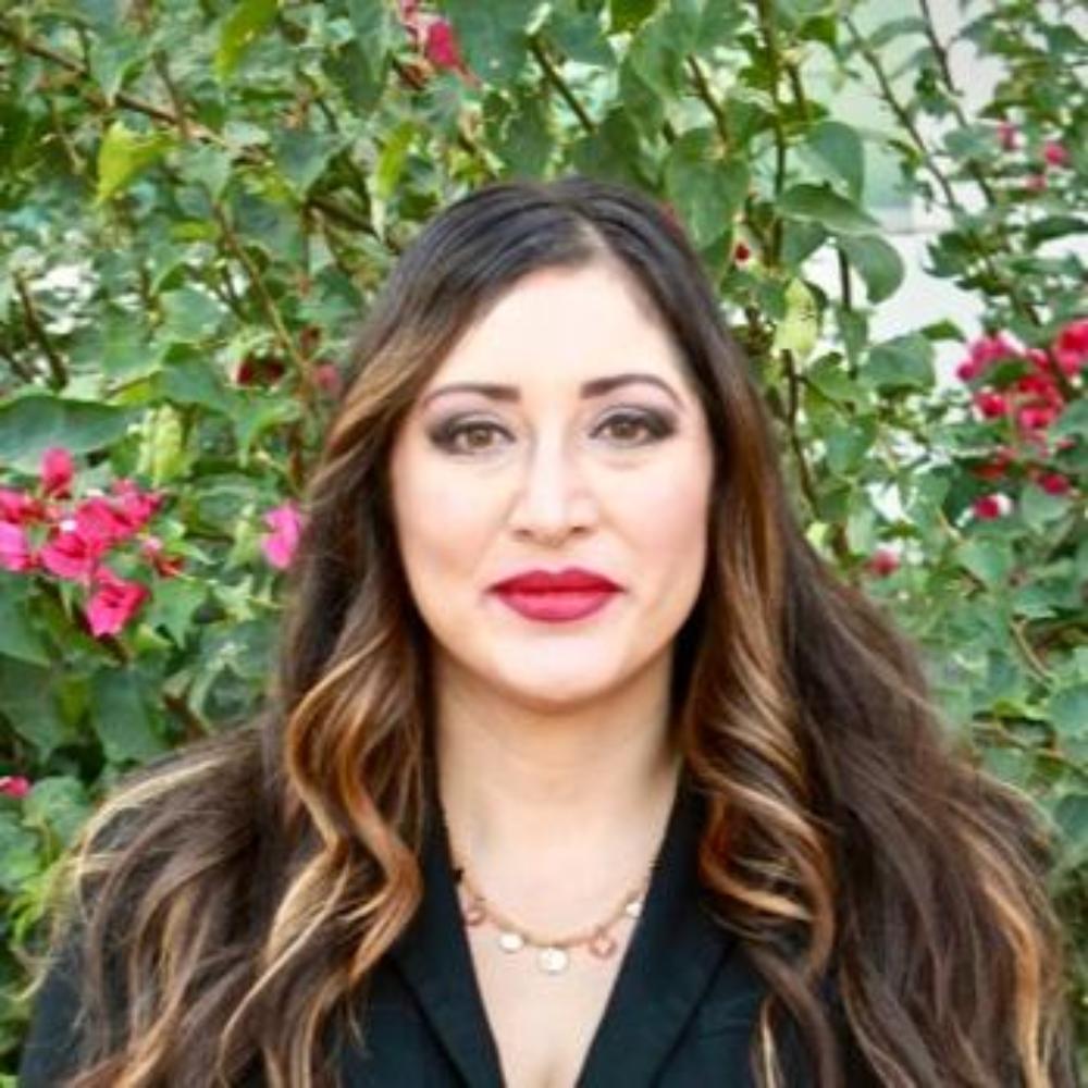 A woman in black attire standing in front of a plant with red flowers.