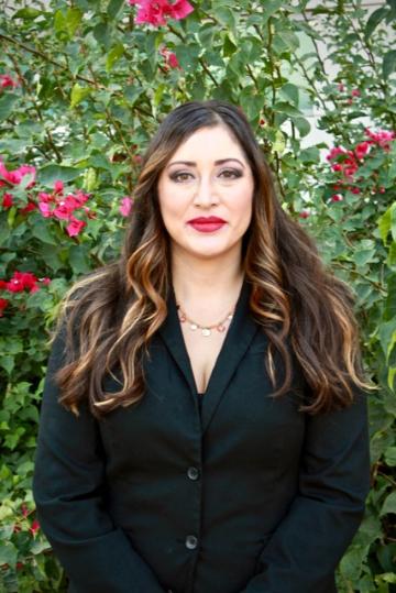 A woman in black attire standing in front of a plant with red flowers.