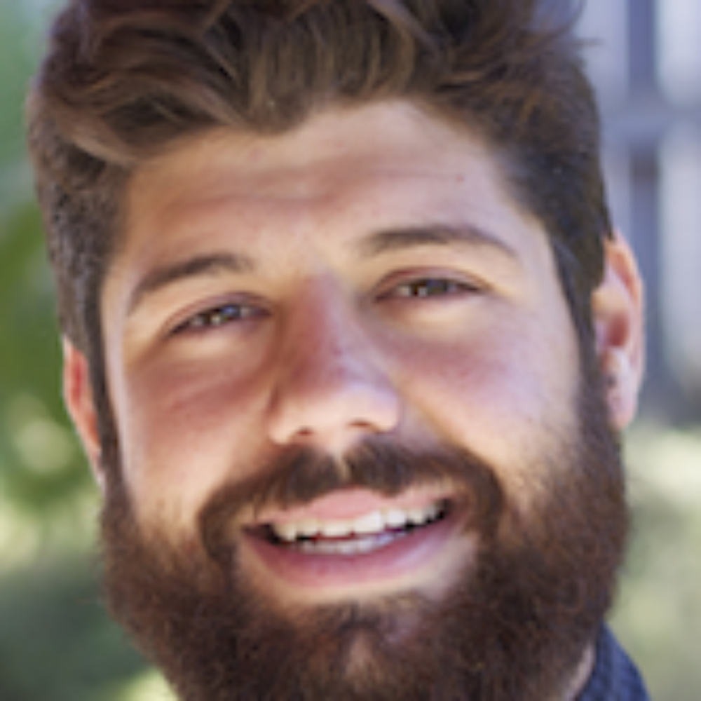 A man with a beard smiling outdoors.