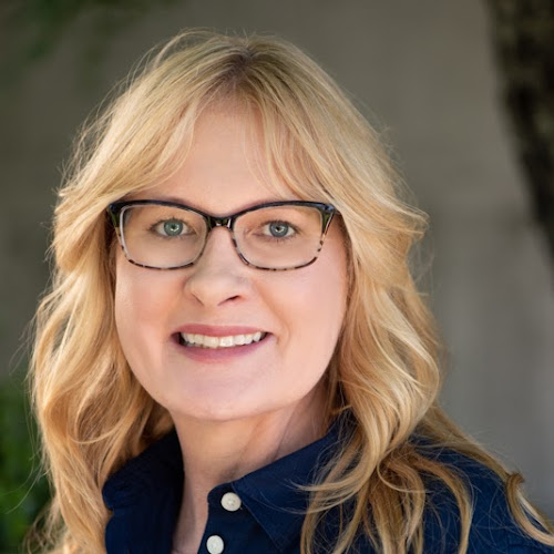 A person wearing glasses, smiling, and standing outside.