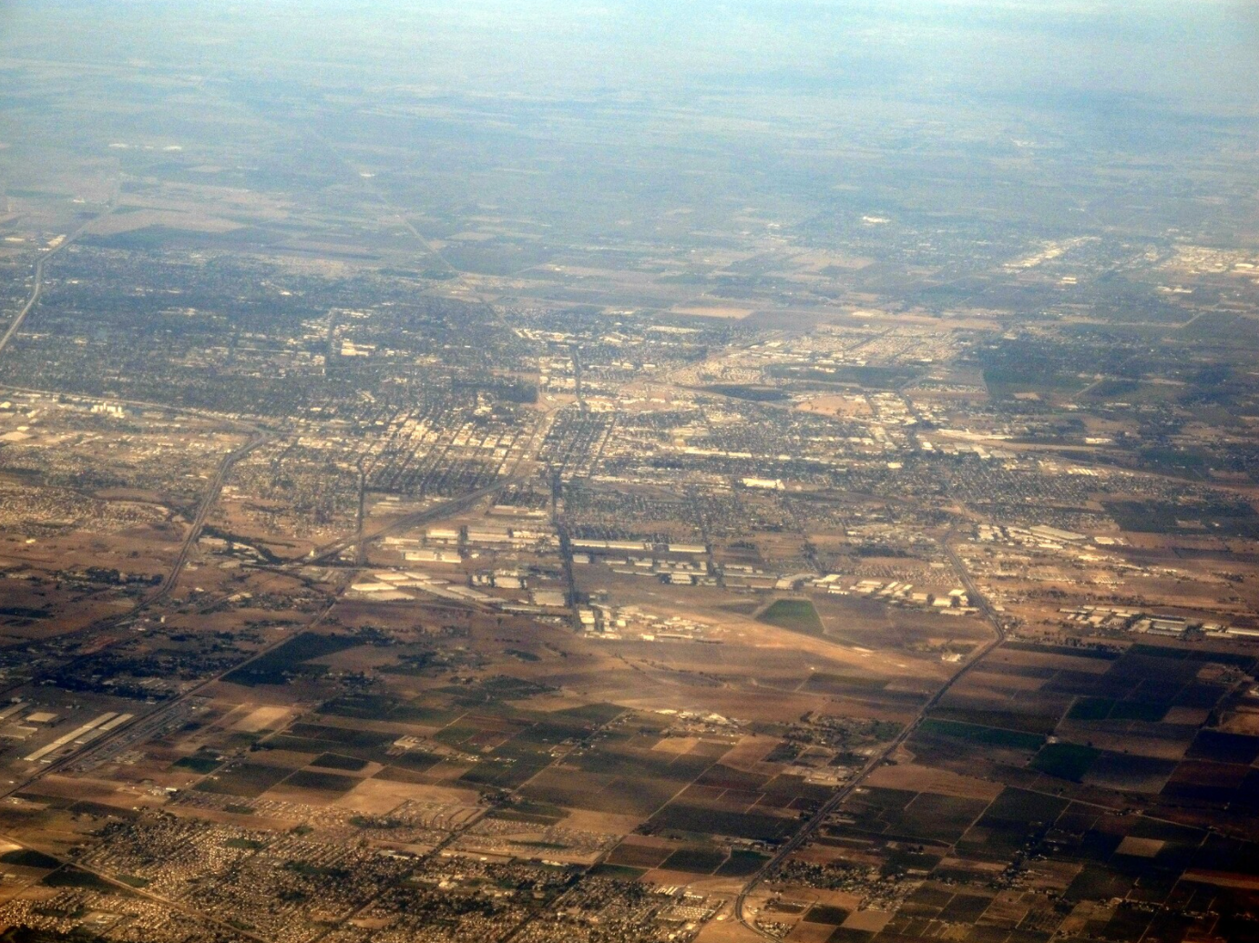 Aerial view of a city and surrounding landscape under a blue sky.