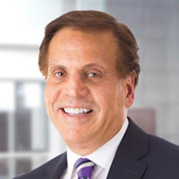 A person smiling in a formal suit with a background of office windows. image link to story