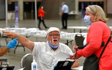 A poll worker wearing PPE directs a voter wearing a face mask to polling station