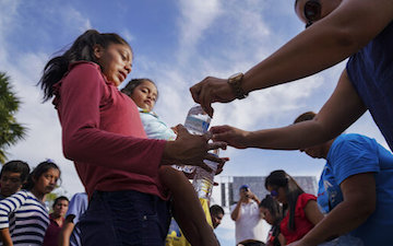 People distributing water bottles in a crowd on a sunny day