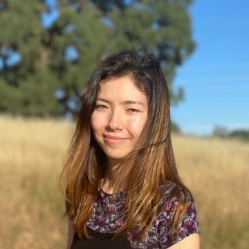A woman standing outdoors with trees and grass in the background.