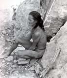 Person sitting against rocks, holding an object.