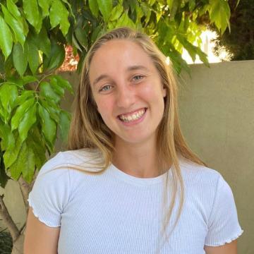 A person smiling in front of green leafy background.