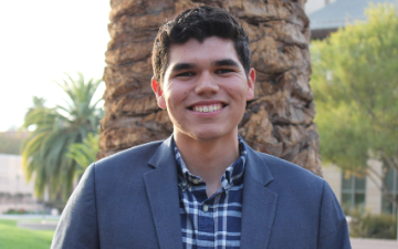 A person in a blazer standing outdoors with a tree in the background.