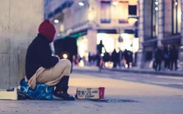 A person sitting beside a building and looking into a street. Photo credit: Ev/Unsplash 