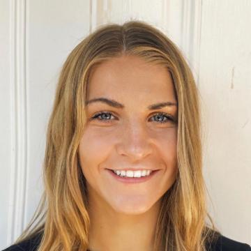 Young woman smiling wearing a black top with a heart pendant necklace.