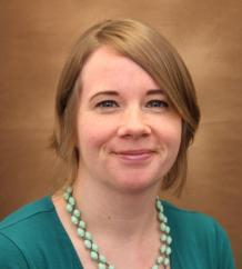 A woman smiling in front of a brown background. image link to story