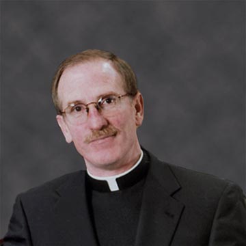 A man in clerical clothing against a gray background.